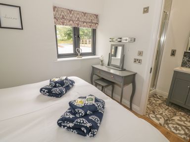 A bedroom with two beds with towels on them a dressing table with a mirror and stool a window and a doorway leading to a bathroom at The Barn in Droitwich Spa