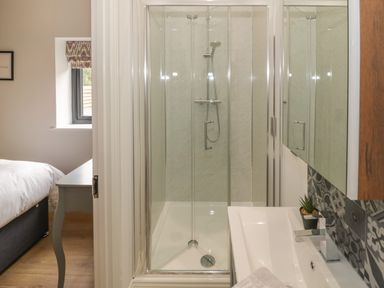A small bathroom with a glass shower enclosure a sink with faucet and a part of a bedroom visible at The Barn in Droitwich Spa
