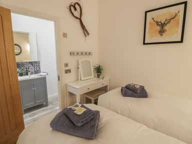 A bedroom with two single beds a white dressing table and a view into a bathroom at The Barn in Droitwich Spa