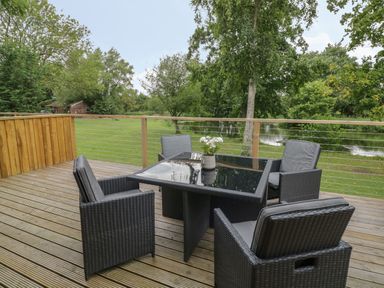 An outdoor deck with a glass table and four chairs overlooking a grassy area and a pond at The Barn in Droitwich Spa