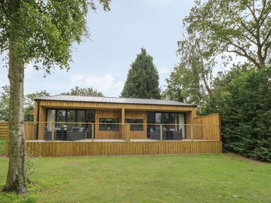 A wooden house with a deck and outdoor seating surrounded by trees at The Barn in Droitwich Spa