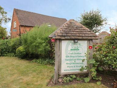 A wooden sign with a tiled roof in front of bushes and a red brick building at Jinney Ring Craft Centre in Droitwich Spa