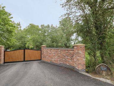 A driveway entrance with wooden gates and brick walls with trees and a sign saying Mill Pond Barns