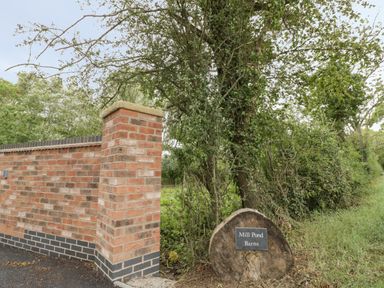 A brick wall next to trees with a wooden sign saying Mill Pond Barns at The Barn in Droitwich Spa