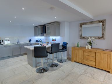 A kitchen with a central island and three black stools next to a wooden sideboard with a mirror above at Low Tide in Weymouth