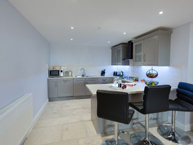 A kitchen with grey cabinets a white countertop black chairs and kitchen appliances at Low Tide in Weymouth