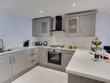 A kitchen with grey cabinets oven stovetop and a counter with wine and glasses at Low Tide in Weymouth