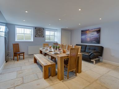 A dining room with wooden table and chairs set for a meal and a black sofa against the wall at Low Tide in Weymouth