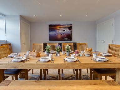 A dining room with a wooden table set with plates cups bread and plants at Low Tide in Weymouth