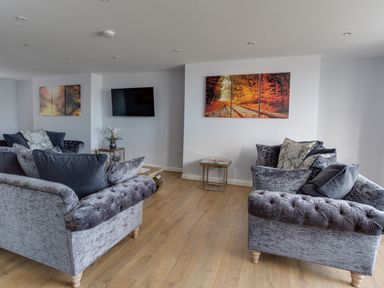 A living room with two grey sofas a wall-mounted TV autumn landscape paintings and a small table with flowers at Low Tide in Weymouth