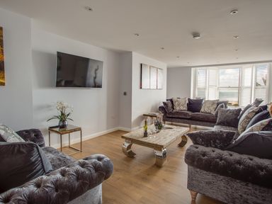 A living room with three dark sofas a wooden coffee table and a wall-mounted TV at Low Tide in Weymouth