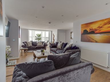 A living room with three sofas a wooden coffee table and a large sunset beach photo on the wall at Low Tide in Weymouth