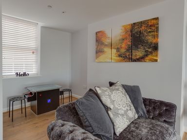 A corner of a room with a dark grey sofa with cushions a small table with stools and a triptych wall art of a forest path at Low Tide in Weymouth