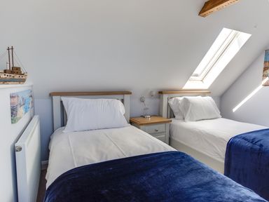A bedroom with two single beds white linens blue blankets skylight window and a nightstand with lamp at Low Tide in Weymouth