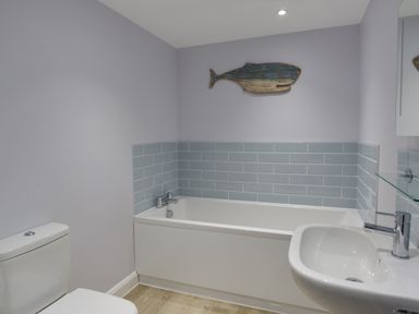 A bathroom with a white bathtub tiled with blue tiles a toilet and a sink with a mirror and a wooden whale decoration on the wall at Low Tide in Weymouth