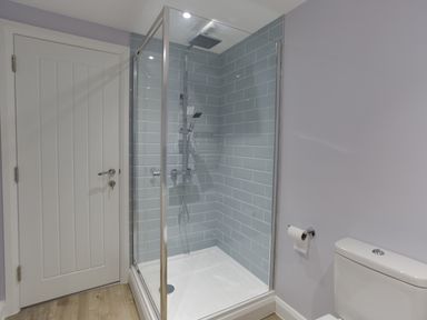 A bathroom with a glass shower enclosure a white door a toilet and a toilet paper holder at Low Tide in Weymouth