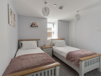 A bedroom with two single beds a nightstand and artwork on walls at Low Tide in Weymouth