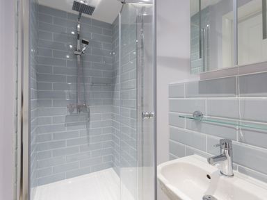 A bathroom shower with blue tiles and a glass door next to a white sink with a faucet and a glass shelf at Low Tide in Weymouth