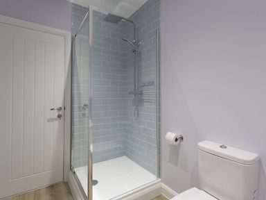 A bathroom with a glass enclosed shower with blue tiles and a white toilet with a toilet roll holder on the wall at Low Tide in Weymouth