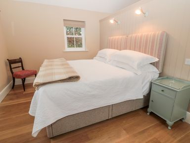 A bedroom with a bed with striped headboard a blanket a small green bedside table and a wooden chair at The Garden Cottage in West Woodburn