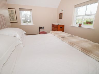 A bedroom with a bed white bedding windows a chair and a wooden chest of drawers at The Garden Cottage in West Woodburn
