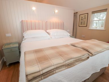 A bedroom with a double bed two beige plaid blankets bedside tables and a window at The Garden Cottage in West Woodburn
