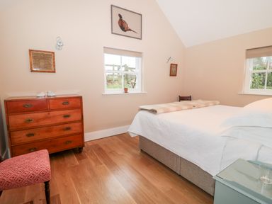 A bedroom with a bed, wooden chest of drawers, chair, two windows, and framed pictures at The Garden Cottage in West Woodburn