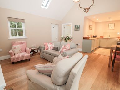 A living room with sofas, an armchair, a small table, and a kitchen in the background at The Garden Cottage in West Woodburn