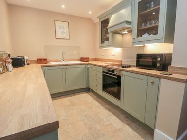A kitchen with green cabinets wooden countertops an oven microwave and sink at The Garden Cottage in West Woodburn