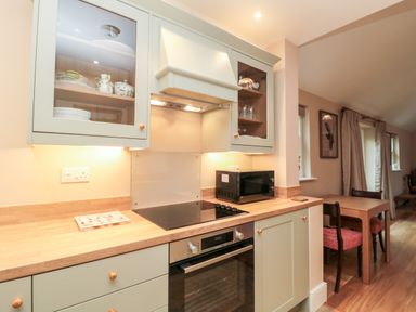 A kitchen with stove oven microwave wooden countertop and cabinets near a dining table with chairs at The Garden Cottage in West Woodburn