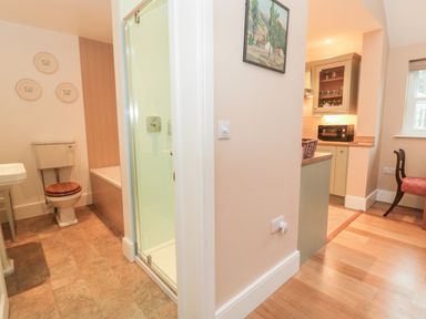 A bathroom with a toilet washbasin and shower next to a kitchen area with cabinets microwave and chair at The Garden Cottage in West Woodburn