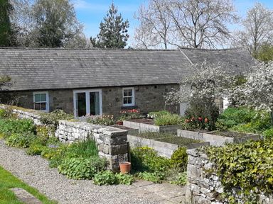 A stone cottage with a slate roof surrounded by raised garden beds and a stone wall at The Garden Cottage in West Woodburn