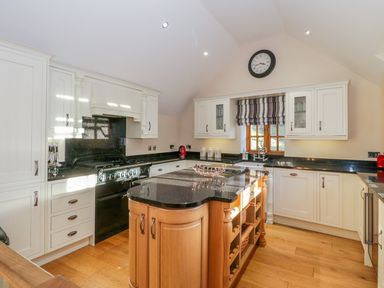 A kitchen with a black countertop island wooden shelves white cabinets and a window with striped blinds at Bwthyn Carregwen in Dwygyfylchi