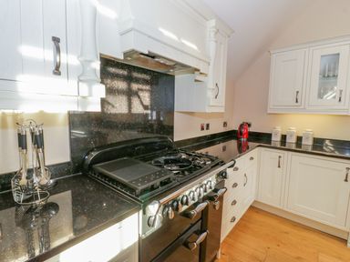 A kitchen with white cabinets black countertops a black stove and kettle at Bwthyn Carregwen in Dwygyfylchi