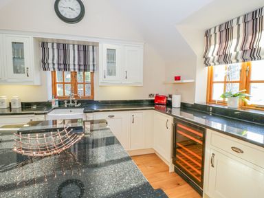 A kitchen with black countertops white cabinets a clock above a window and a wine cooler at Bwthyn Carregwen in Dwygyfylchi