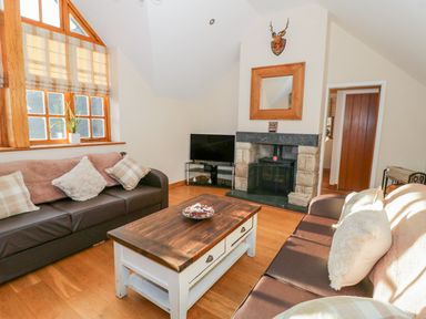 A living room with two brown sofas a wooden coffee table a fireplace and a television at Bwthyn Carregwen in Dwygyfylchi