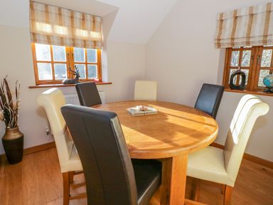 A dining area with a round wooden table and six chairs under two windows with blinds at Bwthyn Carregwen in Dwygyfylchi
