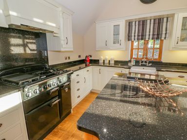 A kitchen with black appliances black countertops white cabinets a wooden floor and a window with striped blinds at Bwthyn Carregwen in Dwygyfylchi