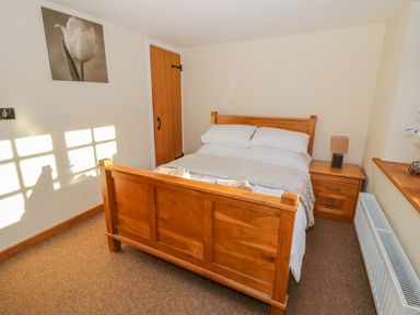 A bedroom with a wooden bed frame bedside table and a wooden door at Bwthyn Carregwen in Dwygyfylchi