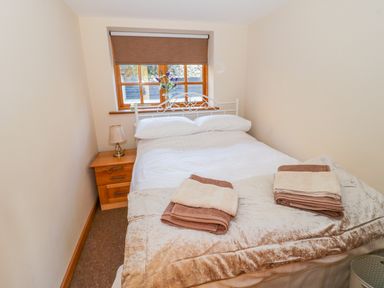 A bedroom with a double bed with white bedding and folded towels on top next to a wooden nightstand with a lamp and a window with a brown blind at Bwthyn Carregwen in Dwygyfylchi