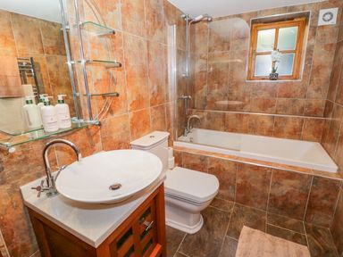 A bathroom with a sink on a wooden cabinet a toilet a bathtub with a shower and a window at Bwthyn Carregwen in Dwygyfylchi