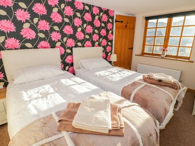 A bedroom with two single beds towels on beds floral wallpaper and a wooden window at Bwthyn Carregwen in Dwygyfylchi