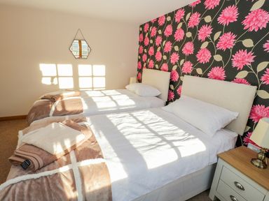 A bedroom with two single beds side by side with white bedding and brown blankets a nightstand with a lamp and a floral wallpaper wall at Bwthyn Carregwen in Dwygyfylchi