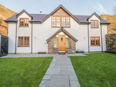 A house with multiple windows and a central wooden door with a stone pathway and a green lawn at Bwthyn Carregwen in Dwygyfylchi