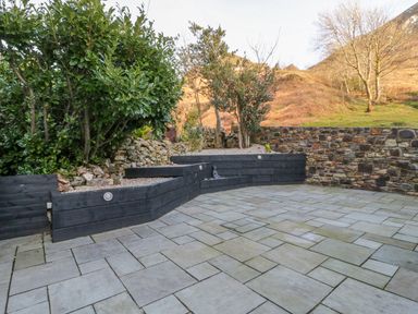 An outdoor patio with stone tiles a raised garden bed with shrubs and stone walls at Bwthyn Carregwen in Dwygyfylchi
