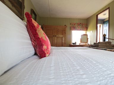 A bedroom with a bed white bedding red pillow wooden wardrobe and dresser with mirror at Crows Cabin in Gloucester