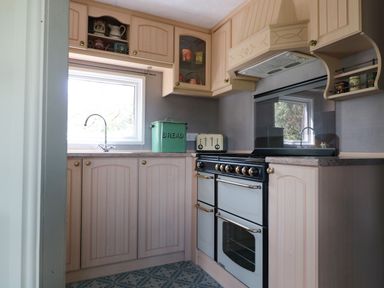 A kitchen with wooden cabinets a black and white stove a green bread box and a window above a sink at Crows Cabin in Gloucester