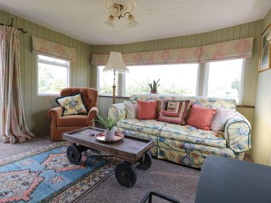 A living room with floral sofa and armchair wooden coffee table and patterned rug at Crows Cabin in Gloucester