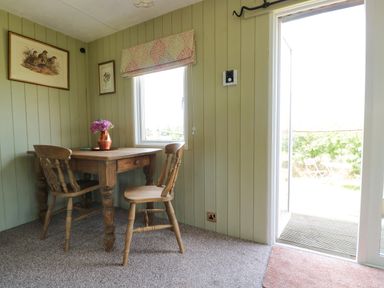 A small dining area with a wooden table and two wooden chairs near a window and an open door at Crows Cabin in Gloucester