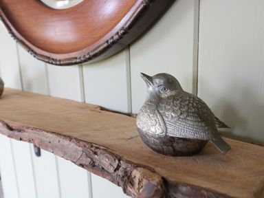 A silver bird sculpture on a wooden shelf with a round framed mirror on the wall at Crows Cabin in Gloucester